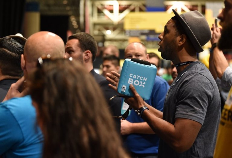 A man is speaking through a blue Catchbox at an event.