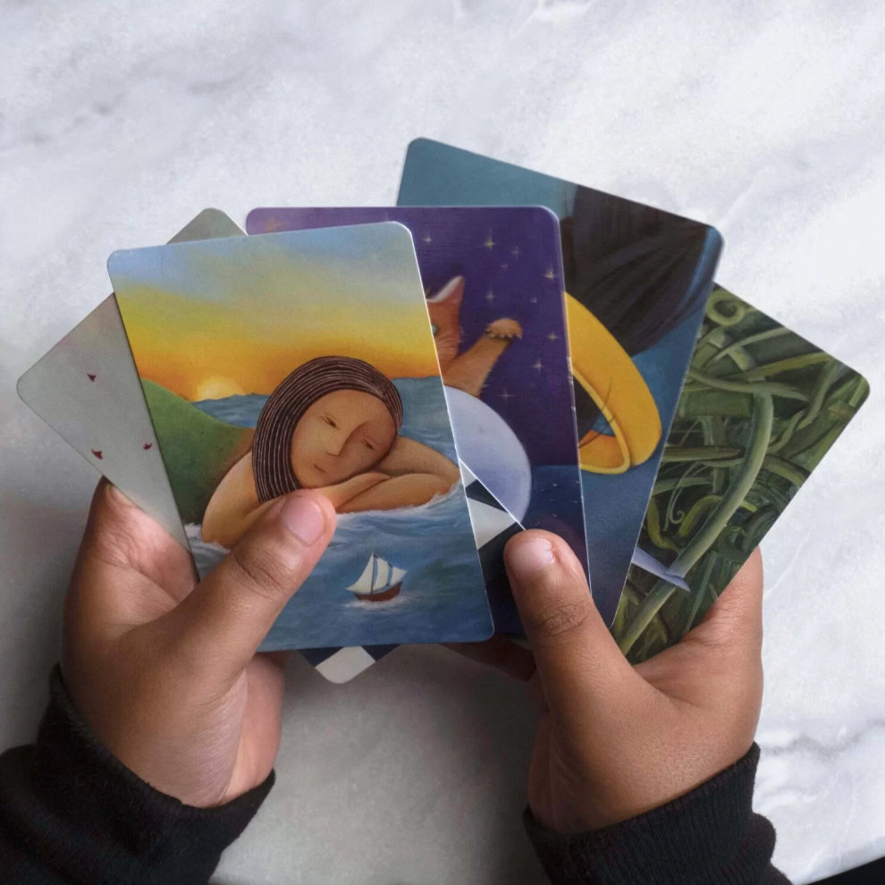 The hand of a player showing 5 cards with beautiful illustrations from the game Dixit.